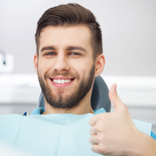 A smiling man sitting in a dentist’s chair and giving a thumbs up
