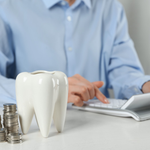 A woman using a calculator next to a large model tooth and stacks of silver coins