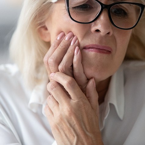 Senior woman with glasses rubbing jaw in pain