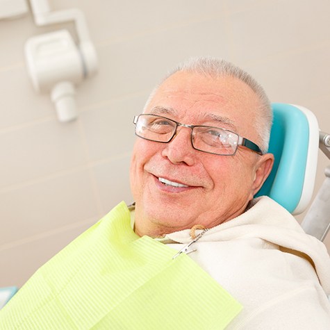 Senior man with glasses sitting in dental chair smiling