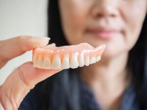 Woman holding a close-up of denture in foreground.